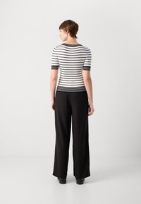Top ajusté à rayures noires et blanches avec des manches courtes, associé à un pantalon large noir taille haute. Tissu lisse, sans motifs visibles.