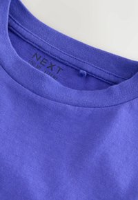 Camiseta de algodón morada con cuello redondo, que presenta una textura suave y etiqueta impresa en el interior. Sin patrones visibles ni detalles adicionales.