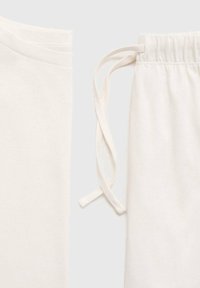 Ensemble de loungewear en coton blanc comprenant une chemise à manches courtes et un pantalon élastique avec cordon de serrage. Texture douce, design minimaliste.