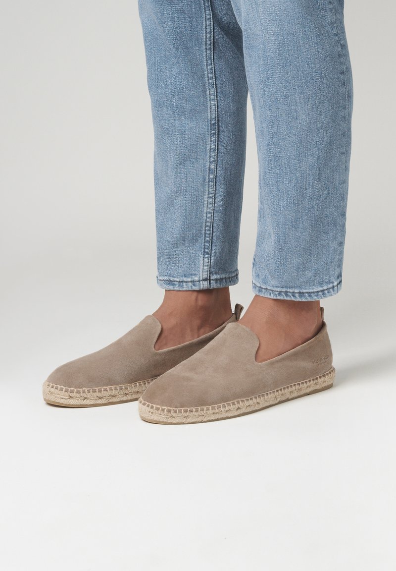 Chaussures slip-on en suede beige avec un bout arrondi, semelle en jute et des détails découpés sur le côté. Portées avec un jean en denim bleu retroussé.