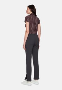 Braunes kurzärmeliges Oberteil mit mehrfarbigem geometrischem Muster, kombiniert mit dunkelgrauer, maßgeschneiderter Hose mit Schlitzen am Saum und weißen Turnschuhen.