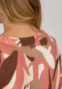 Pull en maille avec un motif floral dans des tons de rose, marron et crème. Encolure côtelée et petite étiquette de marque au dos.
