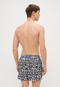 Herren-Badehosen in Schwarz und Weiß mit einem auffälligen Muster aus abstrakten Formen. Elastischer Bund mit einem blauen Markenetikett auf der Rückseite.