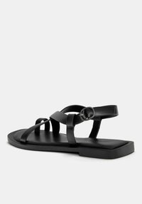Mustat litteät sandaalit, joissa on useita ristikkäisiä straps, valmistettu sileästä nahasta, jossa on suorakulmainen pohja ja säädettävä nilkkasolki.