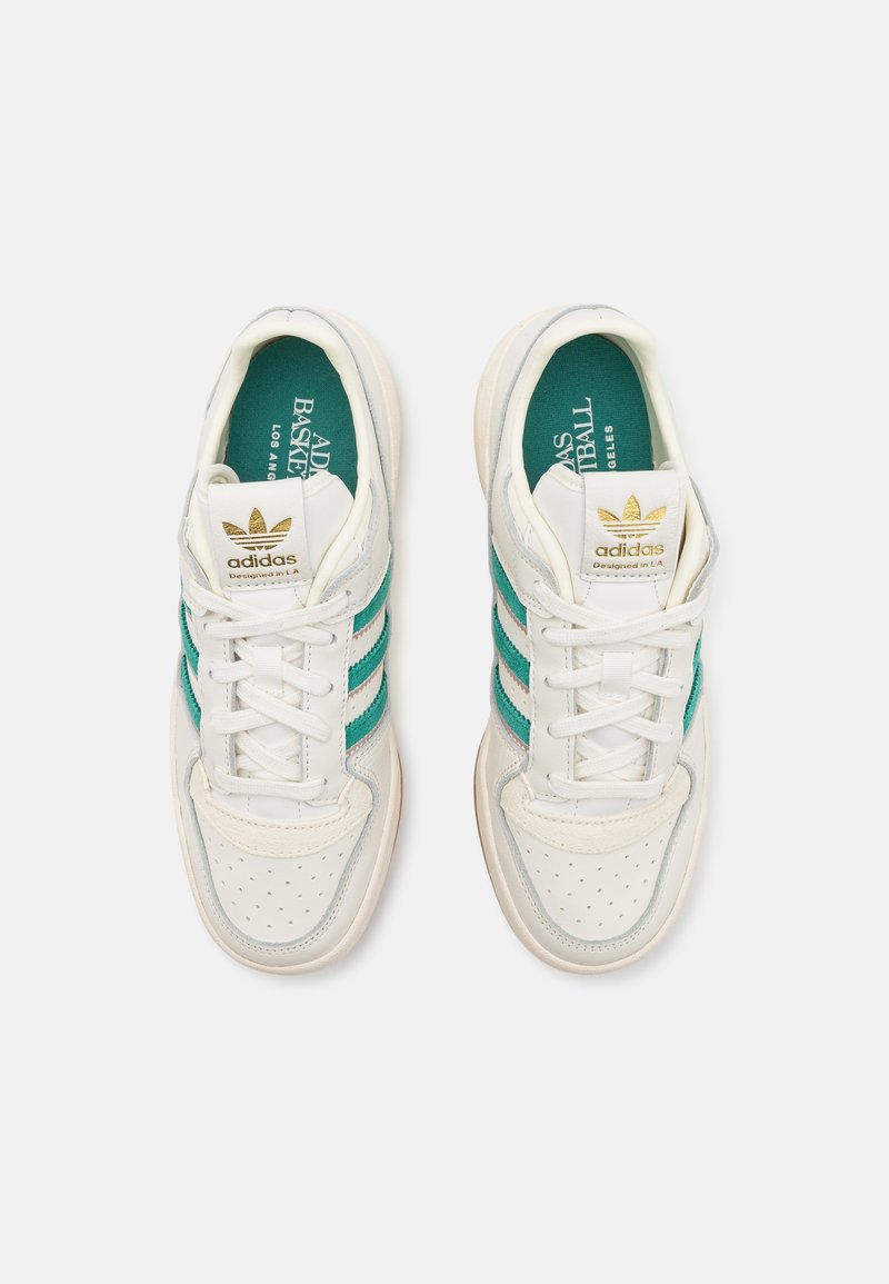 Vita Adidas-sneakers med teal-ränder, perforerat tåområde, vita snörningar och guld Adidas-logotyp på tungan, visade från ovan.