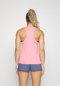 Top deportivo de Nike en un rosa brillante con diseño de espalda nadadora, combinado con pantalones cortos azules. Textura suave, detalle de marca mínimo en la parte posterior.