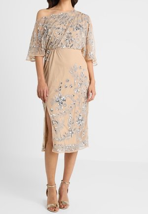 Vestido beige sin hombros con bordado floral plateado, superposición transparente, hasta la rodilla, con una abertura lateral, combinado con sandalias de tiras doradas.