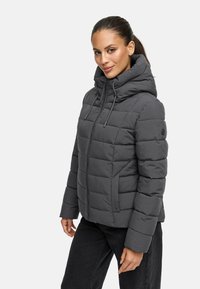 Veste rembourrée grise avec un col montant, fermeture éclair et capuche avec cordon de serrage. Présente un design matelassé et un logo subtil sur le bras.