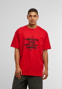 Camiseta de algodón roja con un ajuste holgado, que presenta texto negro que dice "VINE COMO UN REY, ME FUÍ COMO UNA LEYENDA" en una fuente en negrita.
