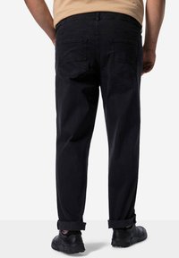 Jeans de mezclilla negra con corte recto, que cuentan con dos bolsillos traseros y puños enrollados. Combinados con calzado negro.
