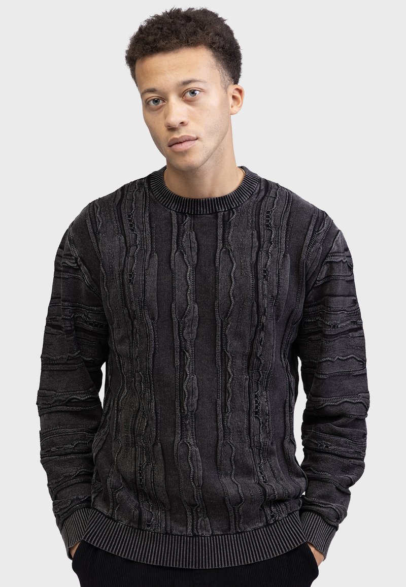 Black sweater with textured vertical stripes, uneven seams, and a ribbed crew neck. Features long sleeves and a fitted waistband.