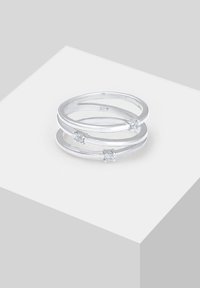 Inel din argint sterling, format din trei benzi interconectate, fiecare având o mică piatră prețioasă transparentă. Suprafață netedă și lustruită, cu un design minimalist.