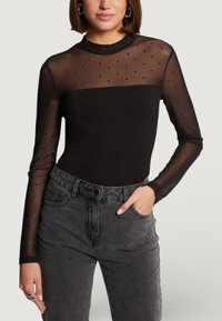 Czarny bodysuit z długim rękawem, z przezroczystymi siateczkowymi rękawami i małymi zdobieniami. Zestawiony z wysokim stanem ciemnoszarymi dżinsami.