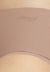 Sloggi saumattomat alushousut pehmeässä beige-kangassa, joissa on sileä pinta ja huomaamaton logopaino. Keski-nousuinen leikkaus ilman näkyviä saumoja.