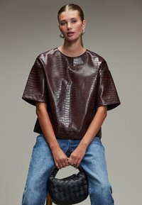 Burgundy faux leather top with a glossy crocodile texture and oversized sleeves, paired with light blue denim and a black woven handbag.