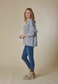 Grauer, gestrickter Pullover mit lockerer Passform, weiten Ärmeln und geripptem Textur, kombiniert mit blauen Skinny-Jeans und beigen Ankle Boots.