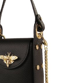 Black leather handbag featuring a gold bee emblem, textured surface, gold hardware accents, and a detachable chain strap.