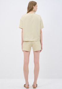 Lys beige kortærmet bluse med løs pasform og rund halsudskæring, parret med strukturerede beige shorts med et subtilt blomstermønster.