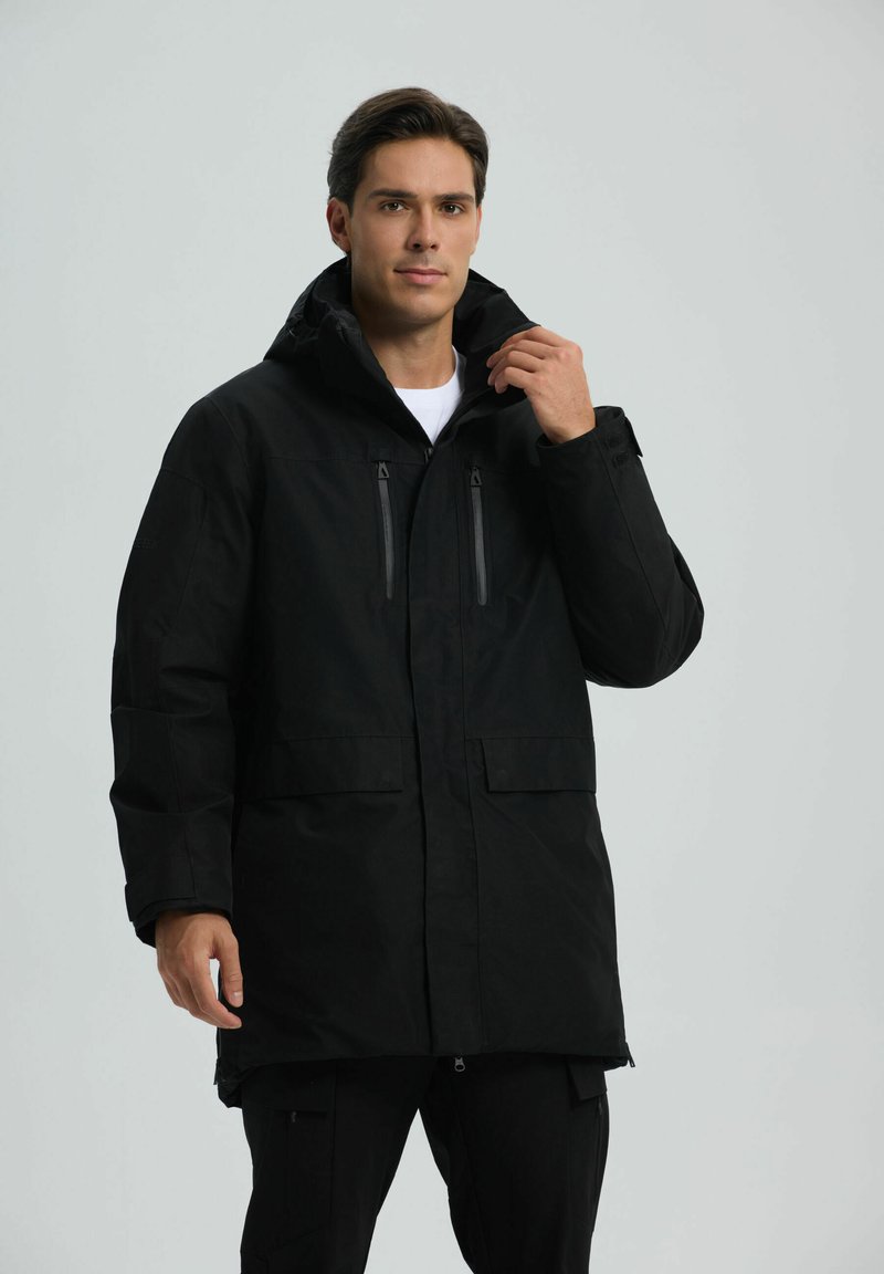 Giacca nera impermeabile con cappuccio, due tasche a zip sul petto, tasche frontali con pattina e polsini regolabili. Design minimalista.