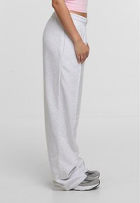 Lys grå, vidde sweatpants med elastisk talje og sidelommer, parret med grå sportsko. Glat stoftekstur.