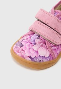 Ροζ παιδικό παπούτσι με πάνω μέρος από υφασμάτινο σχέδιο λουλουδιών, δύο λουριά με βέλκρο και καουτσούκ σόλα σε ανοιχτό καφέ χρώμα. Η κοντινή λήψη αναδεικνύει την υφή και το σχέδιο.