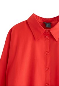 Rød kortærmet skjorte med pointet krave, der har en knappet front, glat tekstur og klassisk pasform. Stoffet ser let ud.