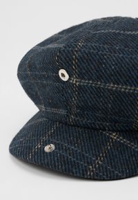 Sötétkék gyapjú keverék sapka barna kockás mintával. Merev karimával és fém díszítésekkel az oldalon az extra részletekért.