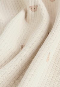 Tissu côtelé de couleur crème avec une texture douce, présentant de petits motifs d'ours en peluche de couleur brun clair.