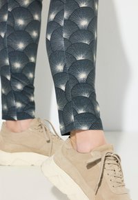 Blauwe leggings met patroon met een ontwerp van lichtgekleurde waaiervormen, gecombineerd met beige sportieve schoenen van suede met een dikke witte zool.