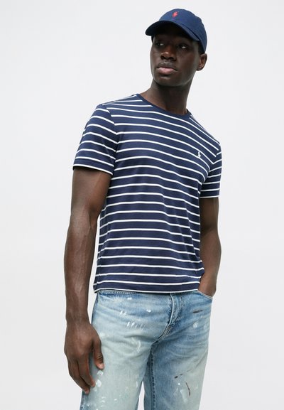 Majica na pruge mornarske plave i bijele boje s okruglim izrezom i kratkim rukavima, u kombinaciji sa svijetlim trapericama s detaljima prskanja boje.