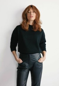 Czarny sweter dziany z wysokim kołnierzem, w połączeniu z czarnymi sk�órzanymi spodniami o wysokim stanie z bocznymi kieszeniami. Prosty, nowoczesny design.