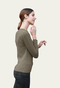 Haut à manches longues vert olive, coupe ajustée, texture douce, encolure ronde, associé à un jean foncé ; la position du modèle montre la vue de profil.
