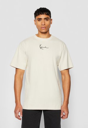 Beige cotton t-shirt with short sleeves and a crew neck, featuring a black cursive logo on the chest. Flat, smooth texture.