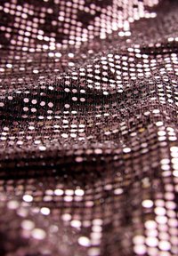 Gros plan sur un tissu marron recouvert de petites paillettes brillantes et réfléchissantes créant une surface texturée et scintillante avec des reflets de lumière.