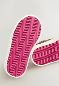 Semelles de baskets présentant un fond en caoutchouc rose texturé avec un motif en zigzag et des bords latéraux blancs. Tissu supérieur coloré partiellement visible.