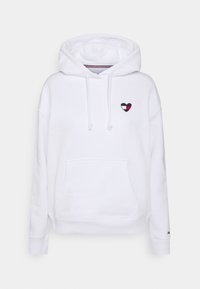 White hoodie with front pocket, drawstrings, and small heart-shaped patch in red, white, and navy on chest, plain background.