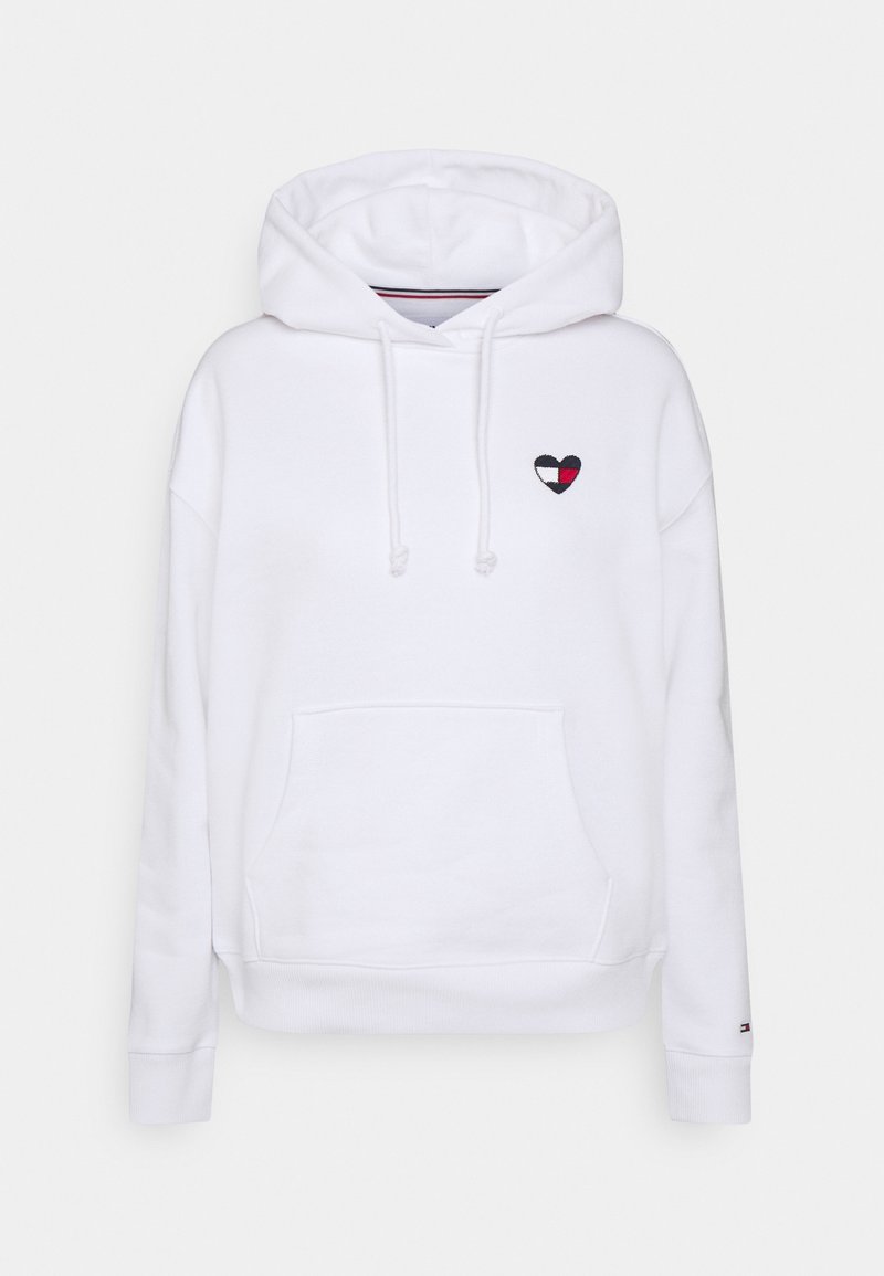 White hoodie with front pocket, drawstrings, and small heart-shaped patch in red, white, and navy on chest, plain background.
