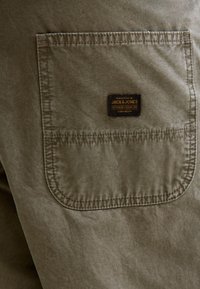 Khaki stoffen zak met een rechthoekige vorm, voorzien van een bruine label met de tekst "JACK & JONES" en decoratieve stikseldetails.