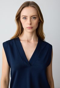 Top senza maniche blu navy con profondo scollo a V e dettagli di cucitura sottili. Realizzato in tessuto morbido, presenta una vestibilità comoda e senza decorazioni.