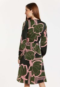 A long-sleeved dress with a dark green base, featuring large pink floral patterns and geometric accents in a smooth fabric.