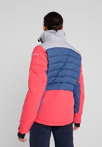 Gesteppte Jacke mit einer Mischung aus Rot, Navy und Grau. Strukturierte Steppnähte auf der Rückseite, hoher Kragen und schwarze Bündchen.