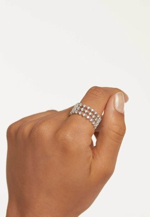 Main avec un ton de peau moyen portant une large bague en argent avec plusieurs rangées de petites pierres précieuses claires et rondes sur l'index.