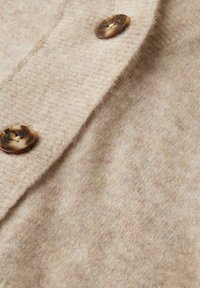 Beige wollen trui stof met een zachte textuur en drie grote, ronde schildpadknopen aan de voorkant.