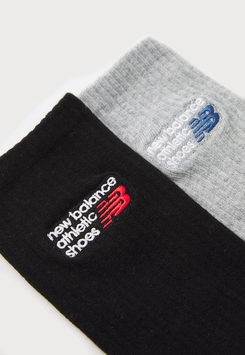 Chaussettes de sport noires et grises avec des logos brodés "new balance athletic shoes" en rouge et bleu, présentant une surface en tricot texturé.