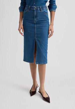 Naine kannab keskmise pikkusega sinist teksaseelikut ees oleva lõhikuga, mida täiendab sinine teksasärk ja tumedad teravate ninaosadega rihmikud.