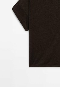 T-shirt marron foncé à manches courtes montrant la manche gauche et le côté sur fond blanc.
