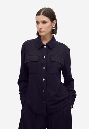 Camisa azul marino de botones con rayas finas, dos bolsillos en el pecho y botones plateados brillantes, hecha de una tela suave y ligera.