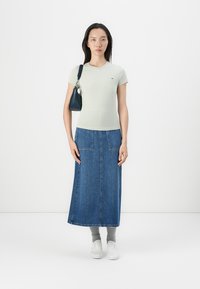 Lys grøn tætsiddende t-shirt, blå denim maxinederdel, hvide sneakers, grå sokker, lille sort handbag. Ingen markante mønstre eller accenter.