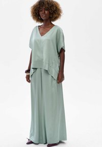 Jasnozielona, satynowa bluzka z dekoltem w serek i zwiewnym krojem, zestawiona z szerokimi, pasującymi spodniami. Prosty, luźny krój, subtelny blask.