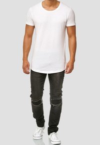Witte T-shirt met ronde hals gecombineerd met zwarte skinny jeans met beschadigde kniedetails, gedragen met witte sneakers. Simpele en moderne stijl.